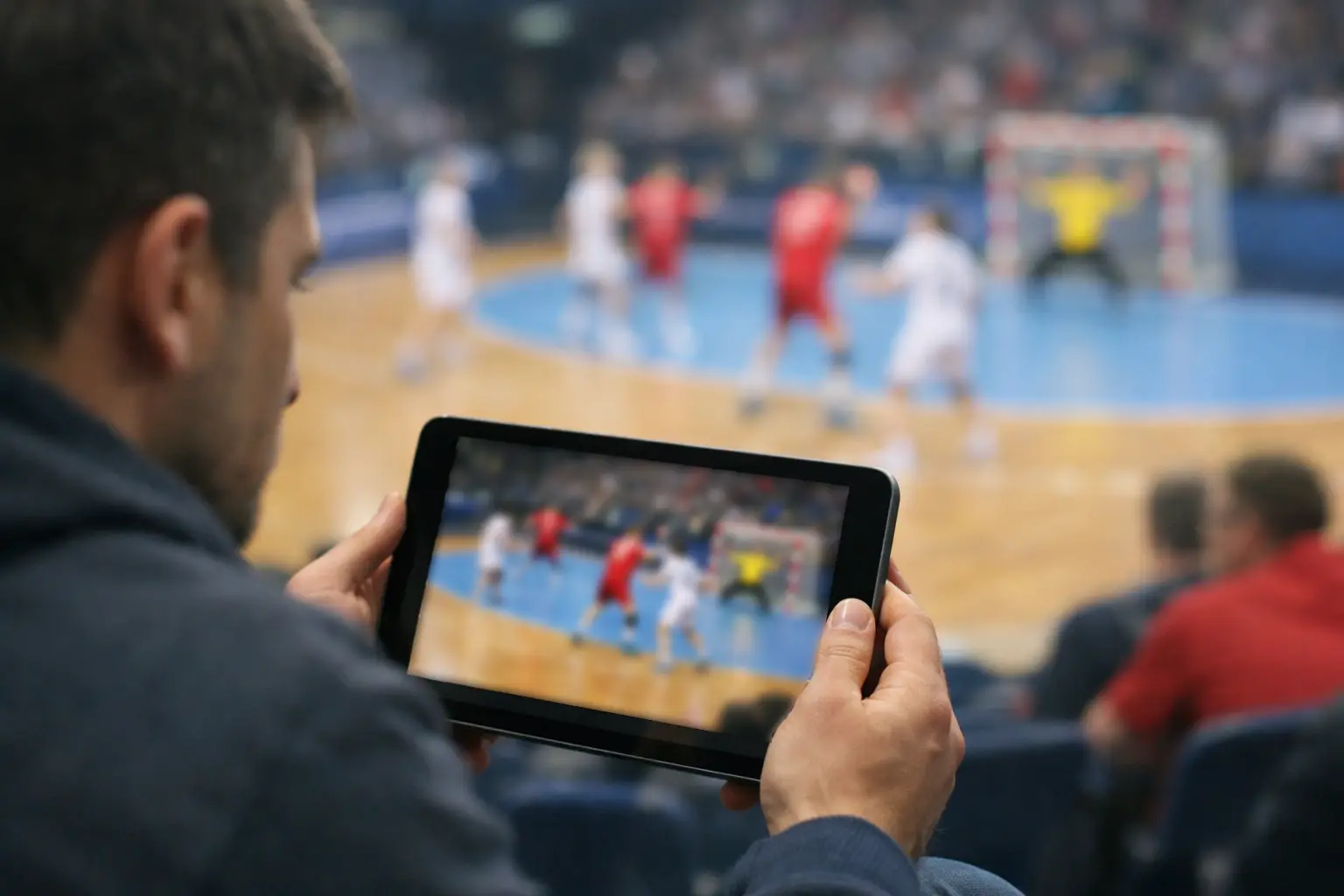 Spectateur suivant un match de handball en direct sur tablette avec application de paris